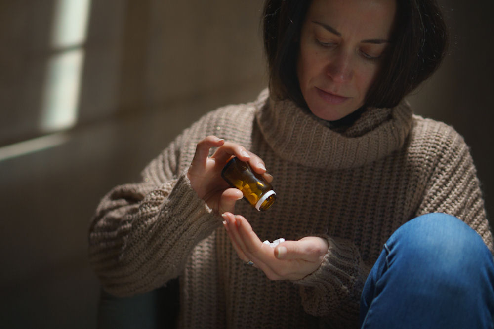 woman wearing sweater and pouring prescription pills into her hand