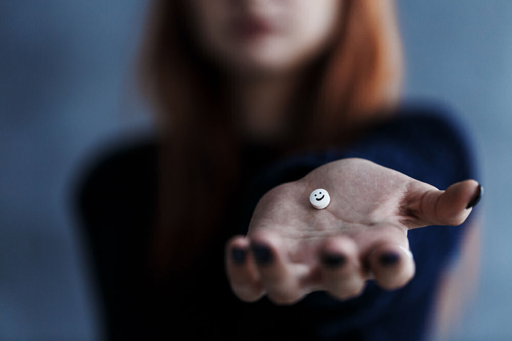 woman holding out her open hand with a small white pill in it