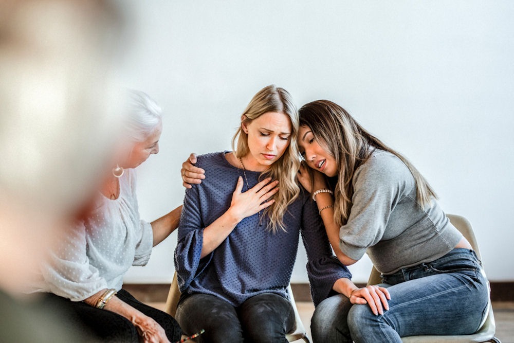 women leaning on each other in group therapy meeting