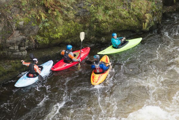 Four people in kayaks are navigating down whitewater rapids.