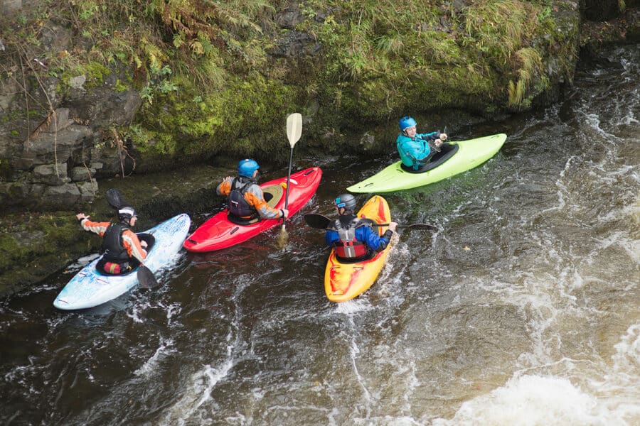 Four people in kayaks are navigating down whitewater rapids.