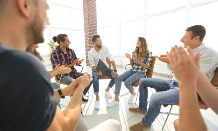 large group sitting in a room with large windows behind them